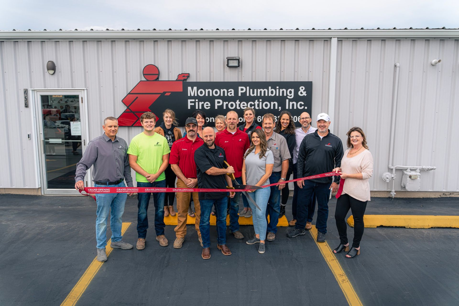 A group of people are standing in front of a building cutting a red ribbon.