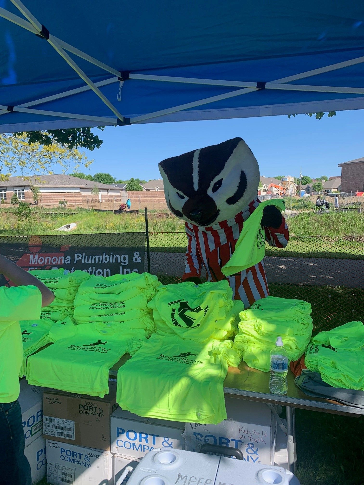 A badger mascot is standing in front of a table full of neon yellow shirts.
