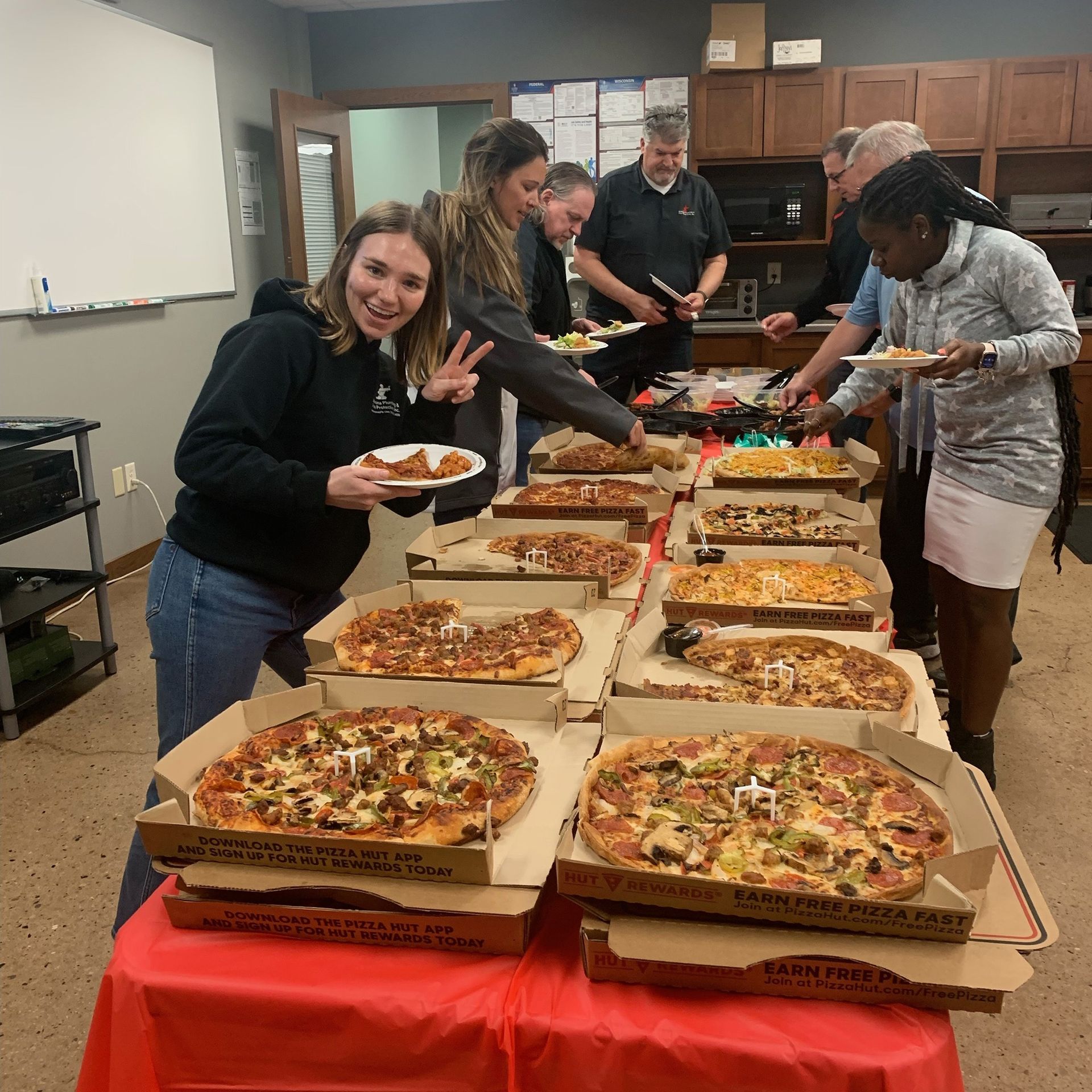 A group of people are standing around a table full of pizzas