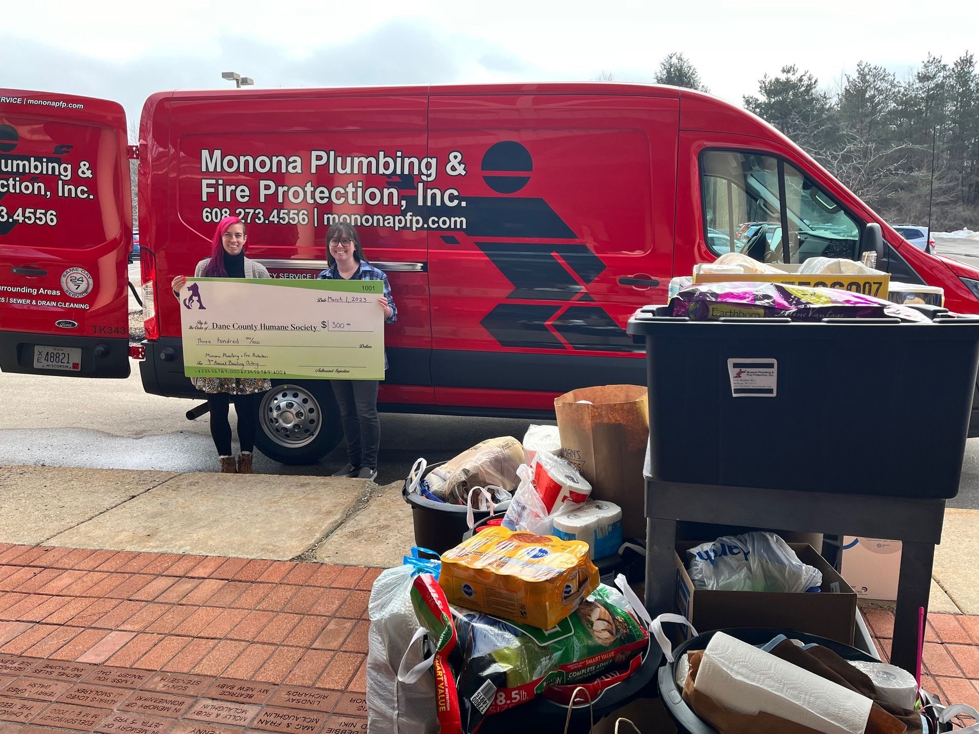 Two people are holding a large check in front of a red van.
