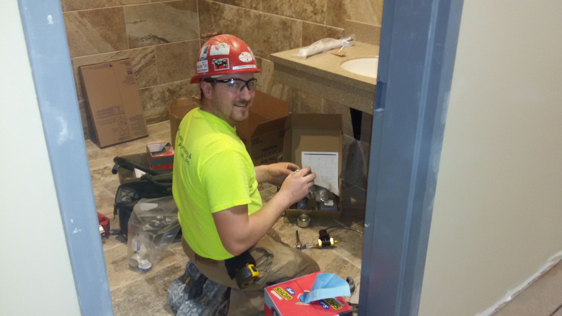 A man wearing a hard hat is kneeling down in a bathroom.