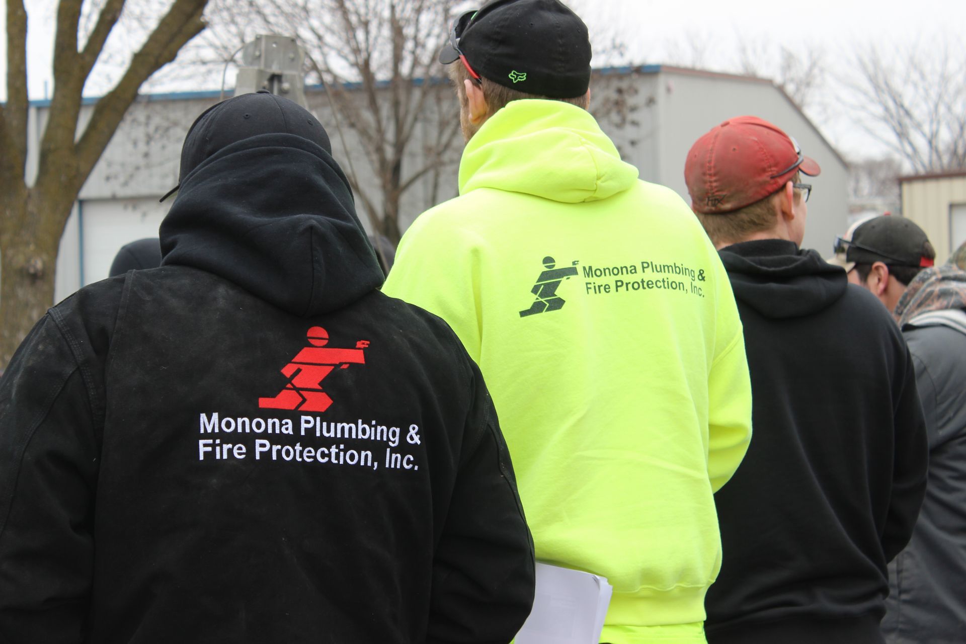 A man wearing a yellow hoodie that says monona plumbing & fire protection inc.