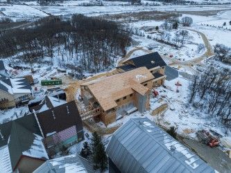 Aerial view of a building construction site in a snowy landscape. Framing and unfinished roofs visible. 
