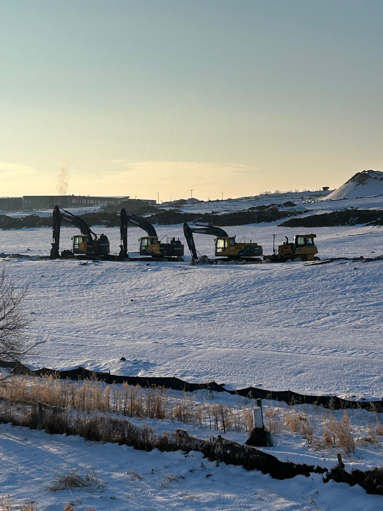 Snow-covered field with four yellow construction vehicles