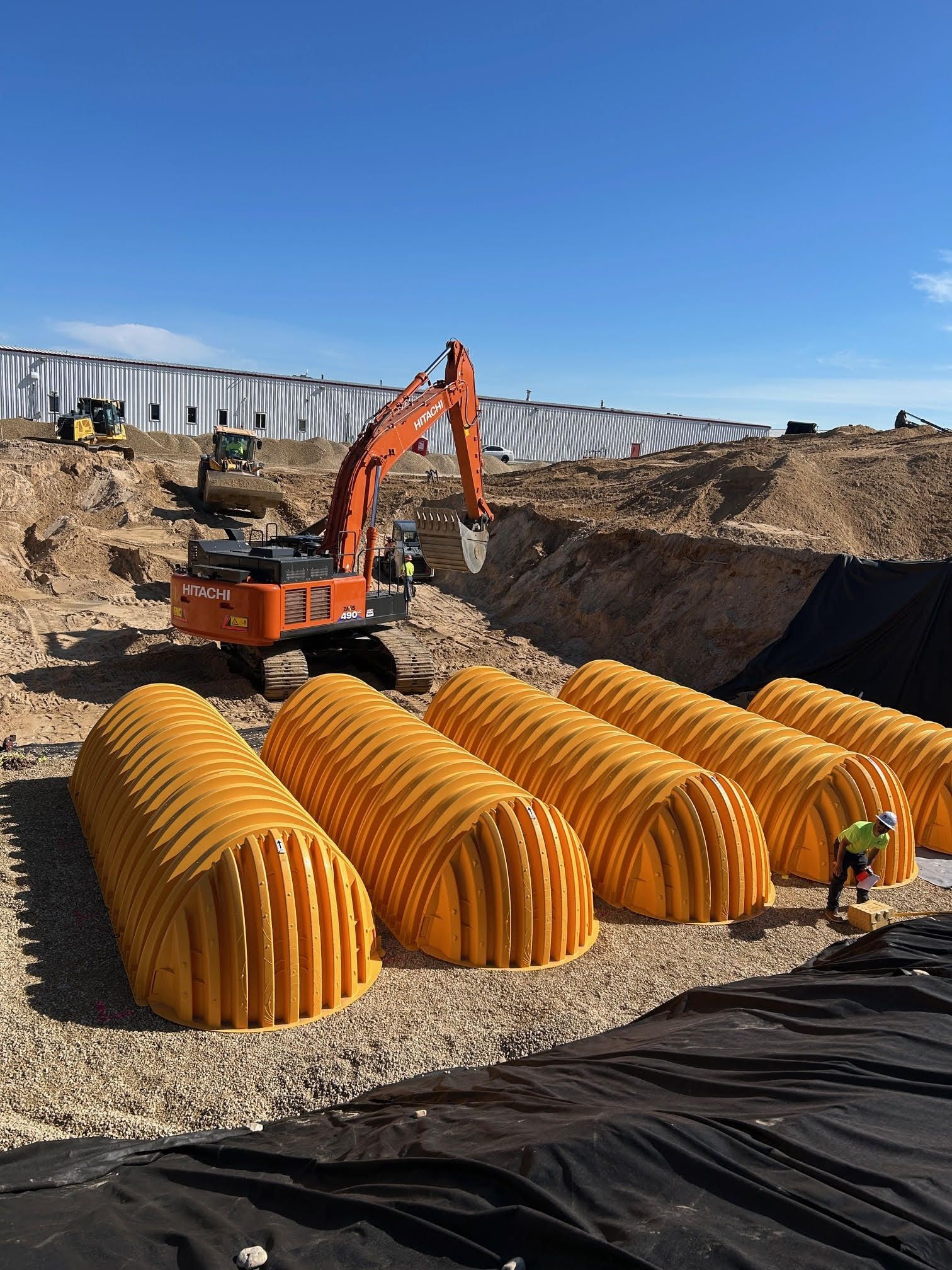 Construction site with orange excavator, arched orange structures, and workers