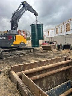 Excavator lifting two green tanks over a trench