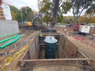 Crane lowering a large green cylindrical container into a trench