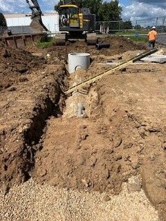 Excavator lifting two green tanks over a trench