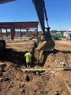 Crane lowering a large green cylindrical container into a trench