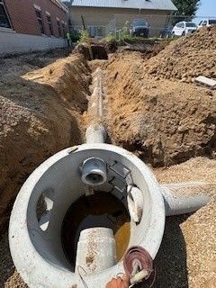 Crane lowering a large green cylindrical container into a trench