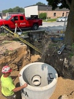 Excavator lifting two green tanks over a trench