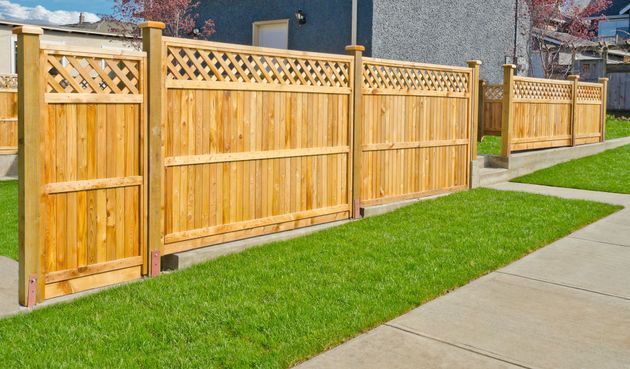 Wooden privacy fence along a green lawn beside a concrete sidewalk in a suburban yard