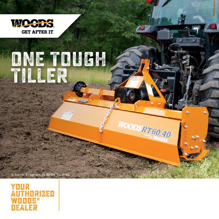 A tractor is driving through a field with a tiller attached to it.