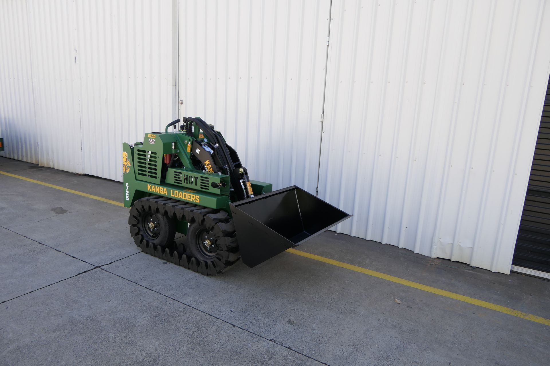 A green tractor with a black bucket is parked in front of a building.