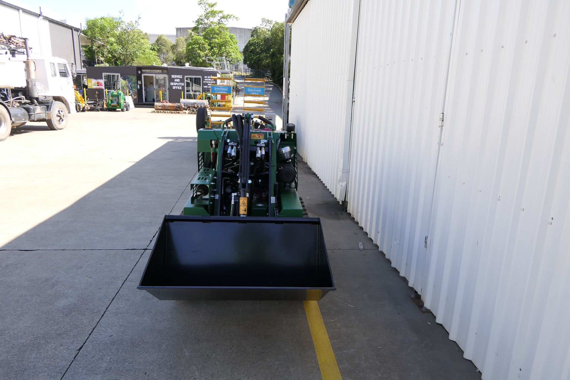 A green tractor with a black bucket is parked in a parking lot.