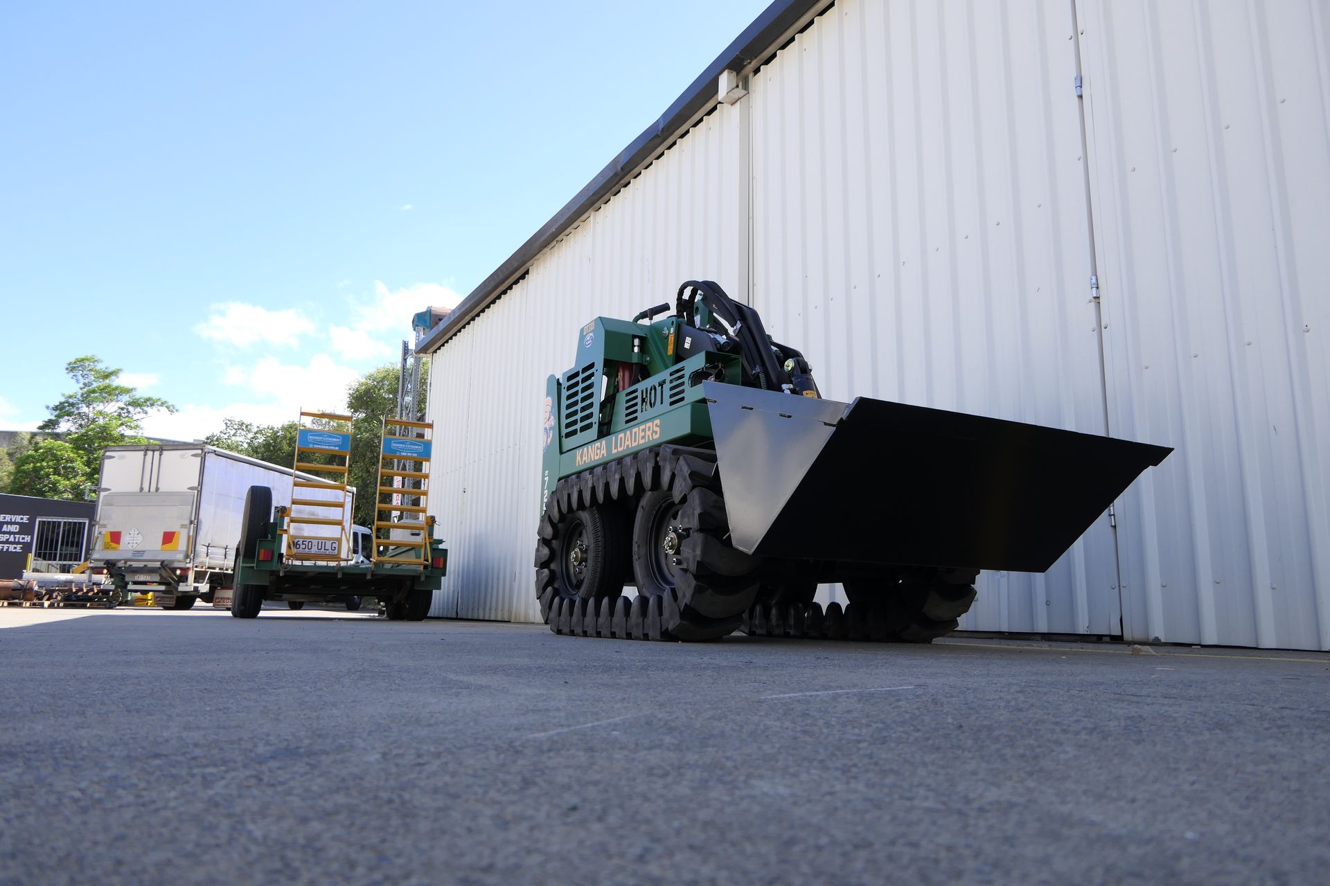 A green tractor with a large bucket is parked in front of a building.