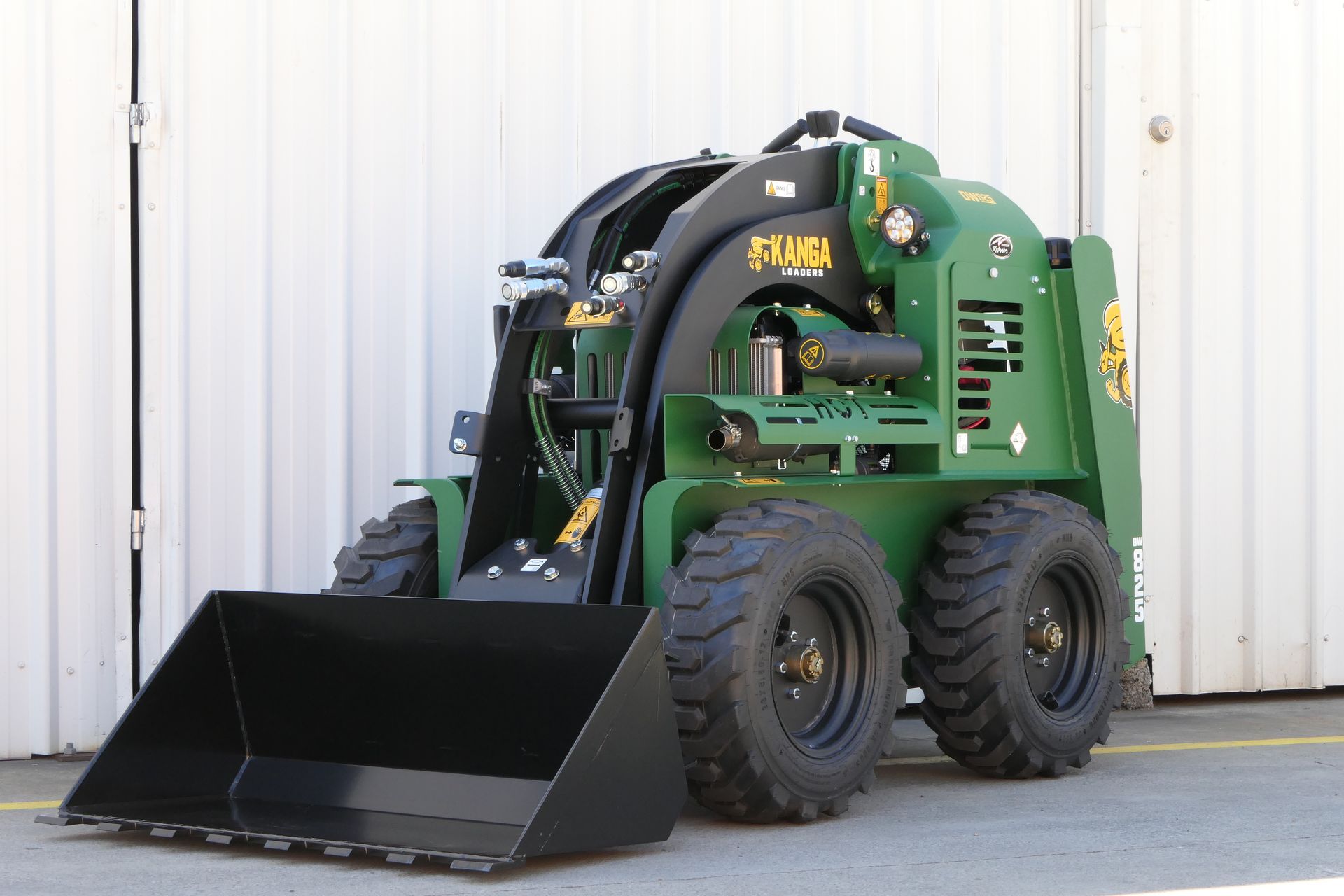 A green Kanga tractor with a black bucket is parked in front of a white building.