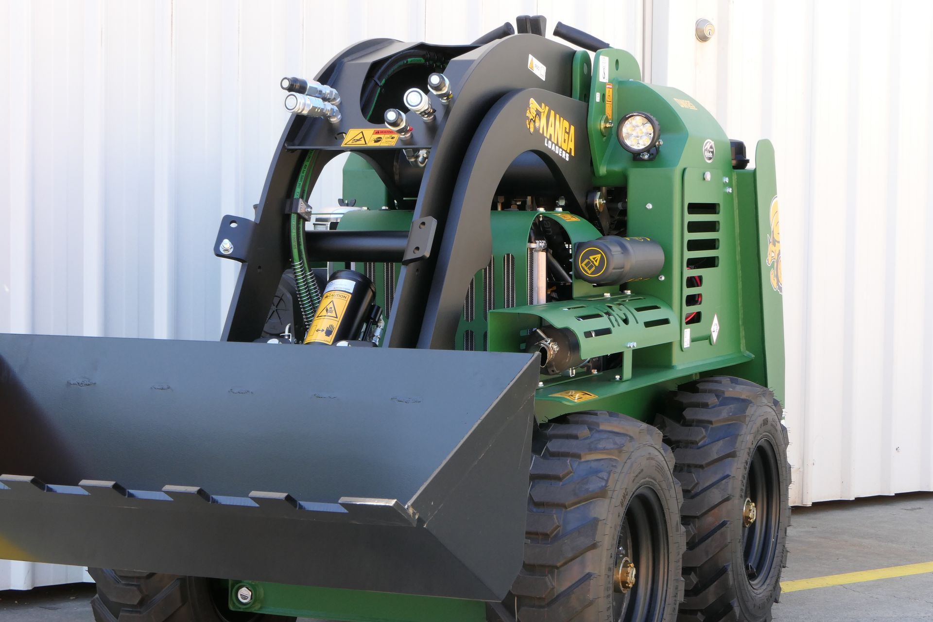 A green Kanga tractor with a black bucket that is parked in front of a white building