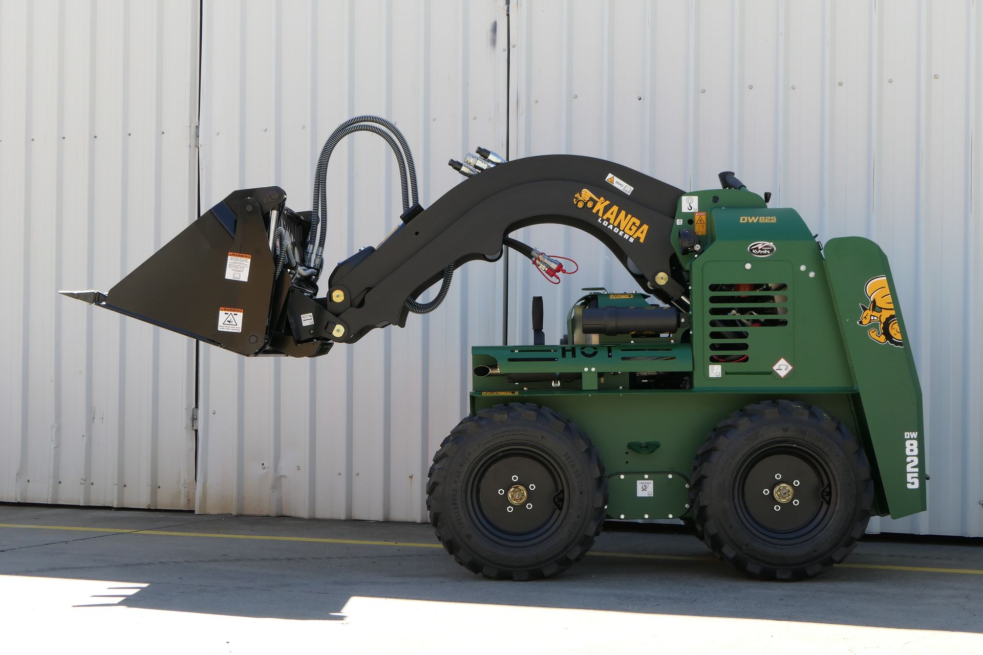 A green Kanga tractor with a black bucket is parked in front of a white building