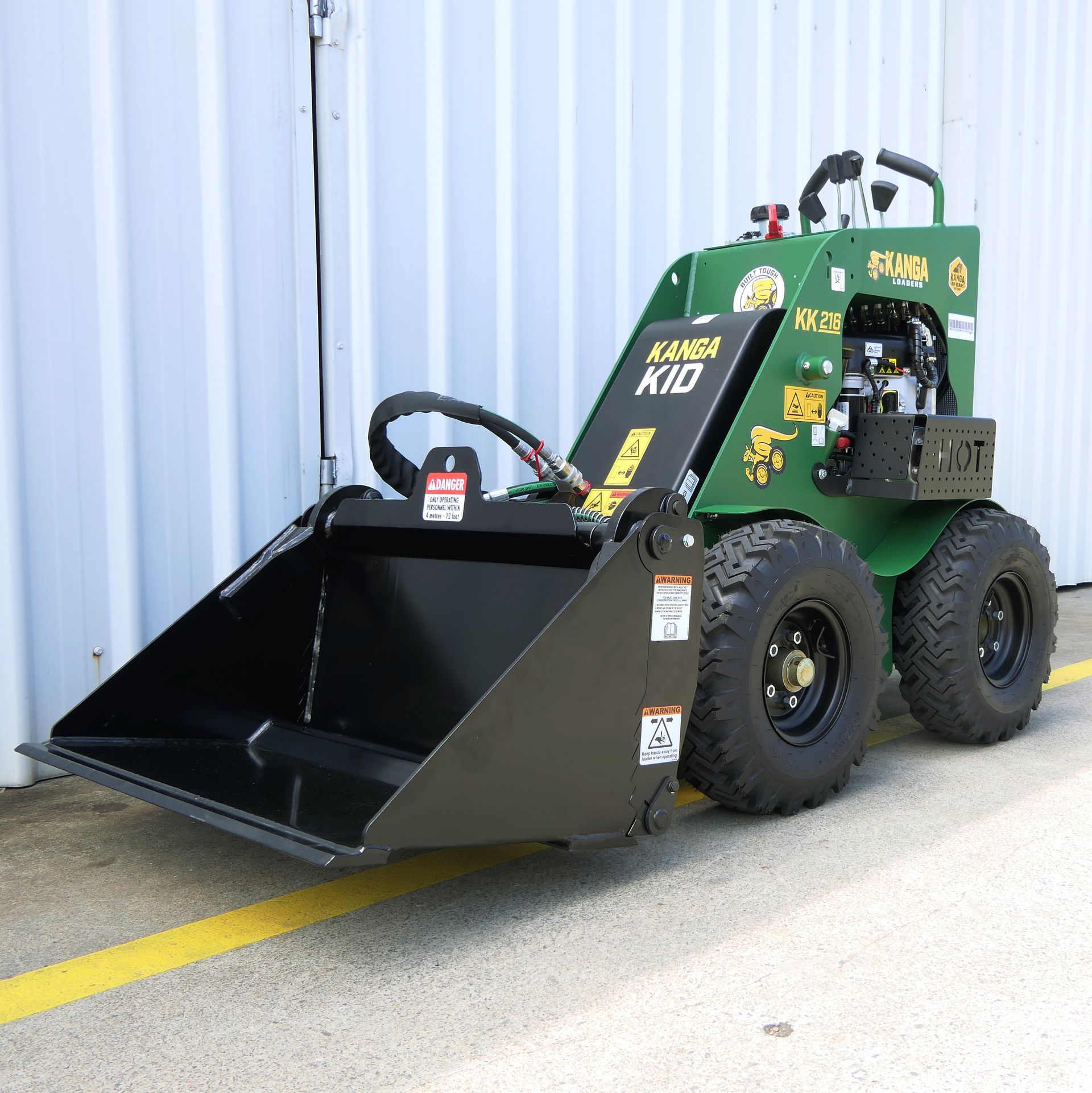 A green Kanga tractor with a black bucket is parked on the side of the road