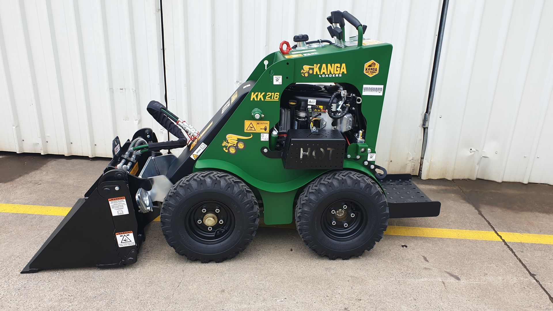 A small green Kanga tractor with a bucket attached to it is parked in a parking lot.