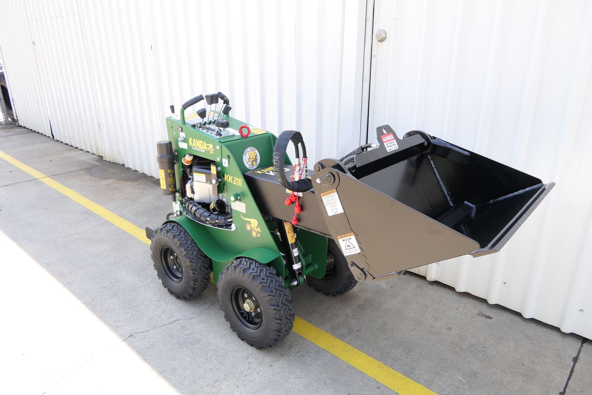 A small Kanga green tractor with a black bucket is parked on the side of the road.