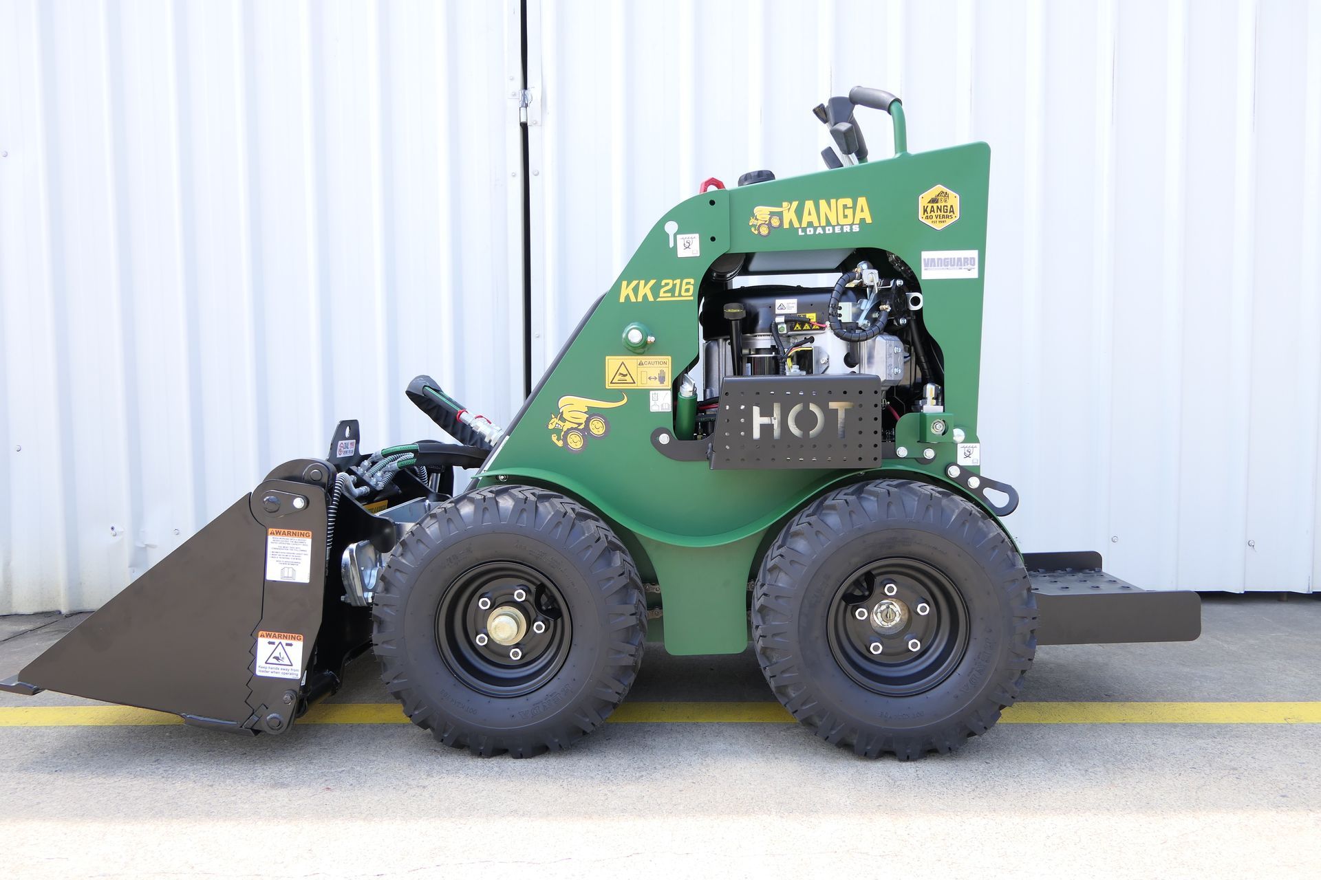 A small green Kanga tractor with a large bucket is parked on the side of the road.
