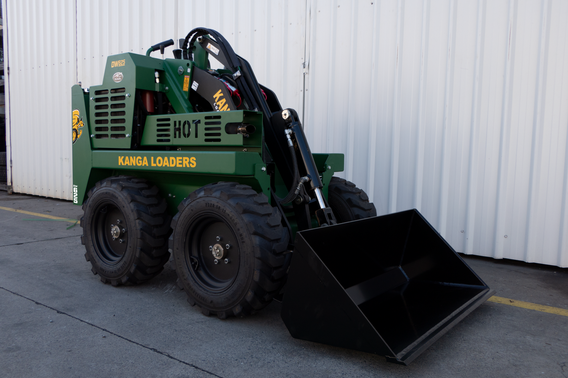 A green Kanga loader with a black bucket is parked in front of a building.