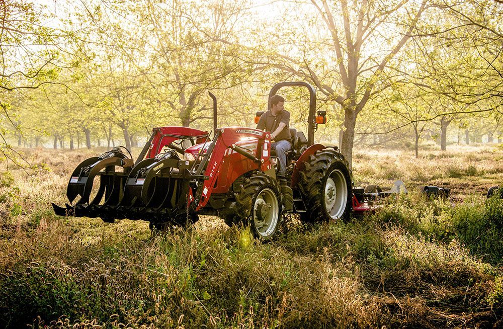 A man is driving a red Massey Ferguson 2600H Series tractor in a field.