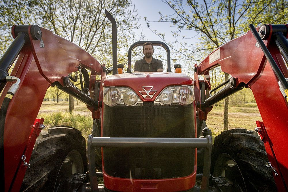 A man is driving a red Massey Ferguson 2600H Series tractor in a field.