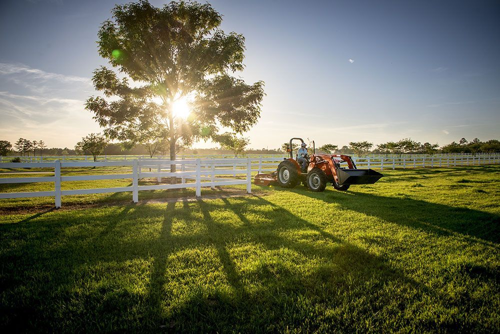 A Massey Ferguson 2600H Series tractor is parked in a grassy field next to a white fence.