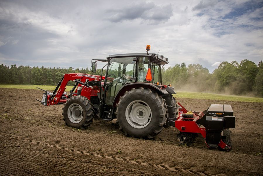 A red tractor is plowing a field with a plow attached to it