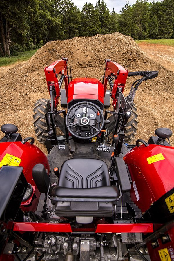 A red tractor is parked in front of a pile of dirt