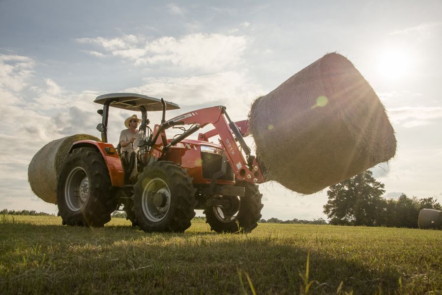 A tractor is carrying a bale of hay in a field