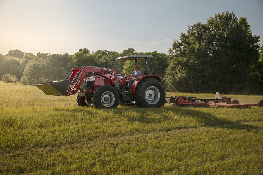 A red tractor is driving through a grassy field with a trailer attached to it