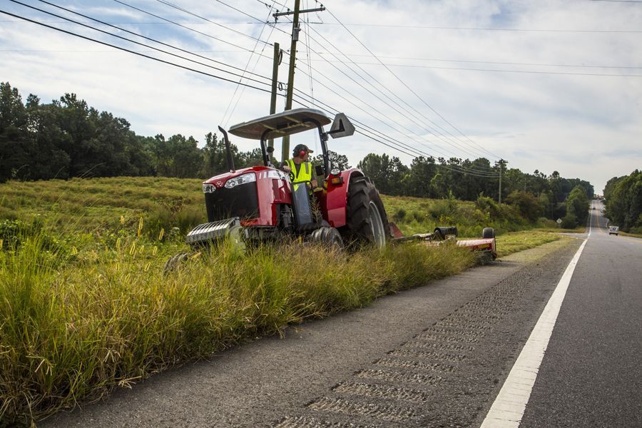 A man is driving a tractor down the side of a road