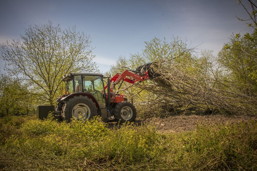 A red tractor is carrying a pile of branches in a field