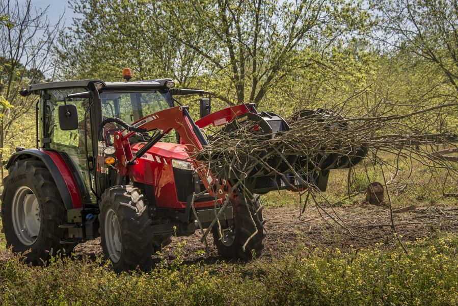 A red tractor is carrying a load of branches in a field