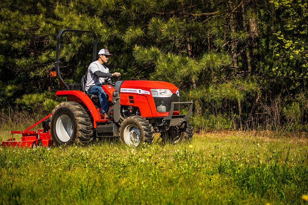 A man is driving a red tractor through a grassy field