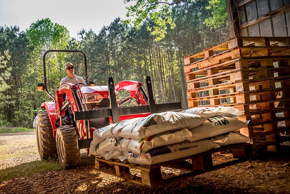 A man is driving a tractor with a pallet of bags on it