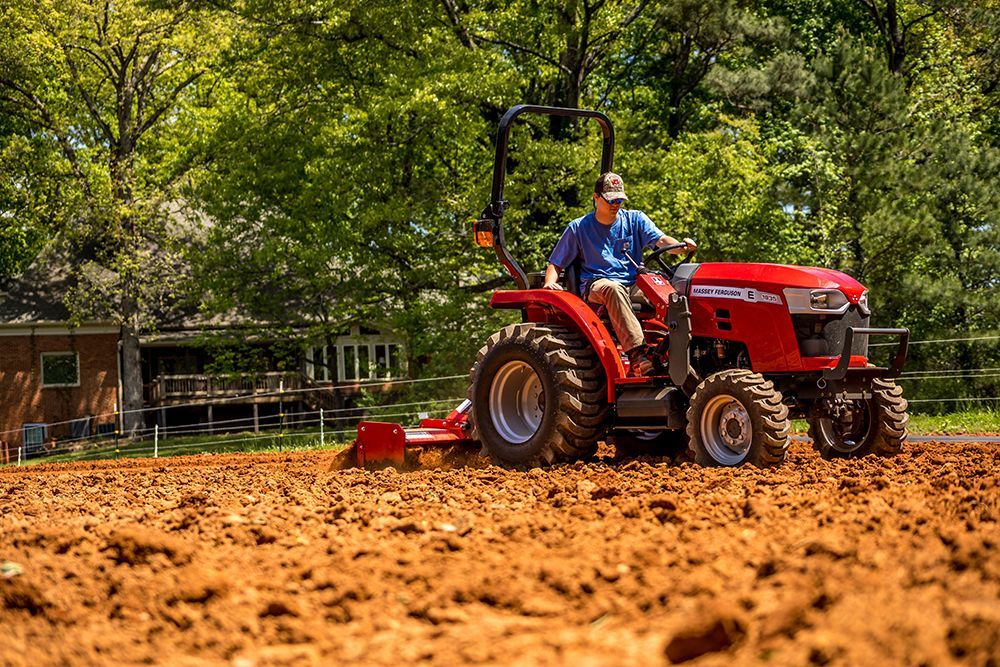 A man is driving a small tractor through a dirt field
