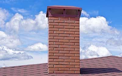 A brick chimney on top of a roof with a blue sky in the background.