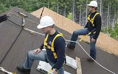 Two men wearing hard hats and harnesses are working on a roof.