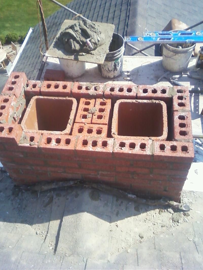 A brick chimney is being built on a roof