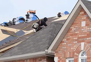A man is working on the roof of a brick house.
