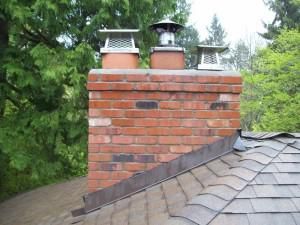 A brick chimney on top of a roof with trees in the background.
