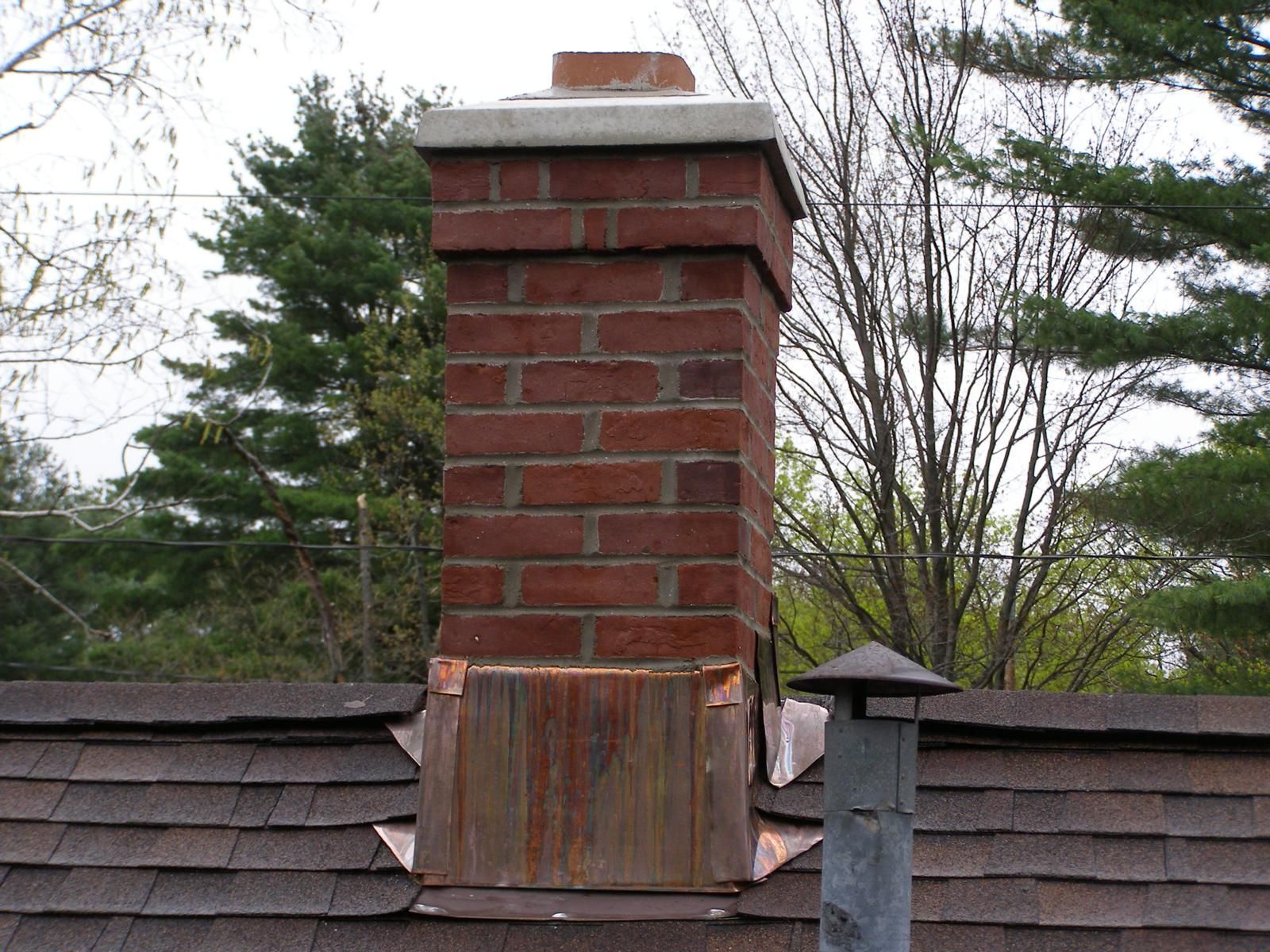 A brick chimney on top of a roof with trees in the background