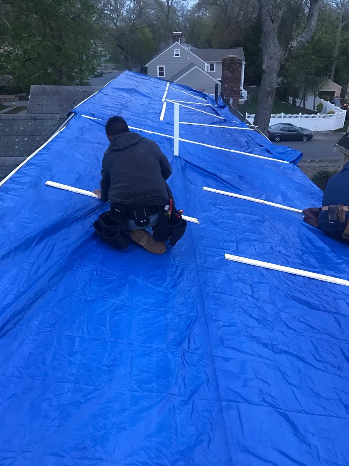 A man is kneeling on a blue tarp on top of a roof.