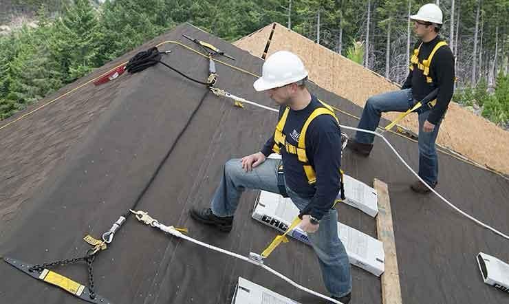 Two men wearing hard hats and harnesses are working on a roof.