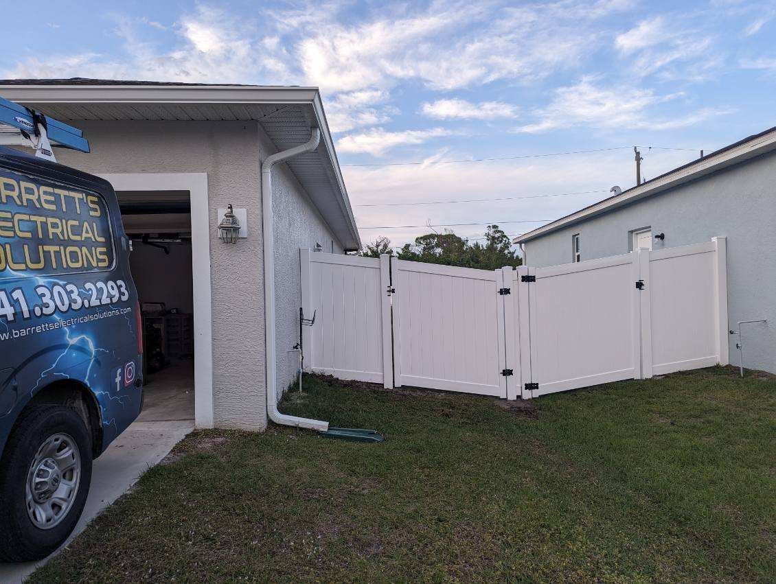 White vinyl fence around a backyard. Garage and electrical van in the foreground. Cloudy sky.